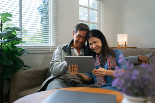istock Retired elderly couple sits on couch using tablet together and relax in their home. Senior Activity Concept 1992080140