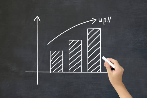 istock Child's hand drawing upward bar graph on black board 1992115450