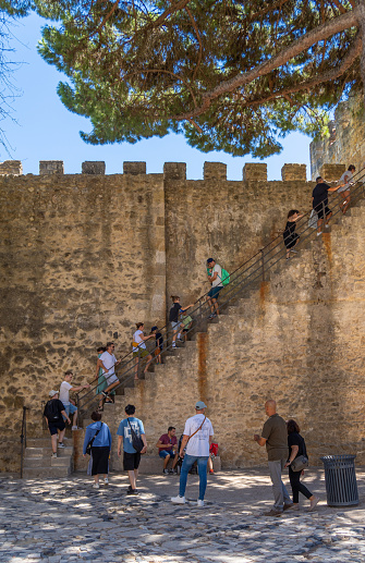 Tourists and families climbing the stairs of the walls of St. George's Castle in Lisbon on a sunny day.