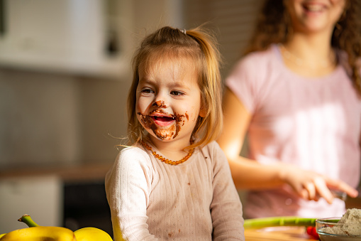 Little girl with chocolate on her face is sitting in the kitchen