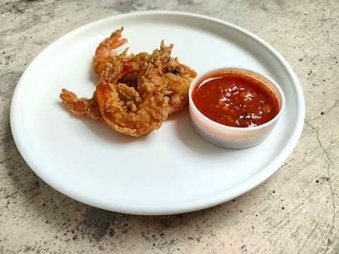 Crispy fried prawns on a white plate with spicy chili sauce