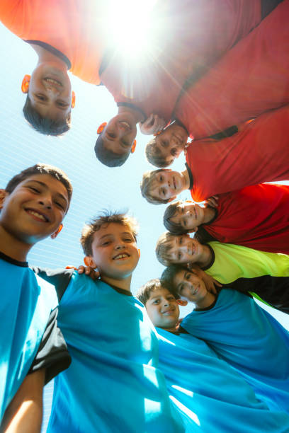 Group of young soccer players in a huddle, showcasing teamwork and youthful energy under the sun.