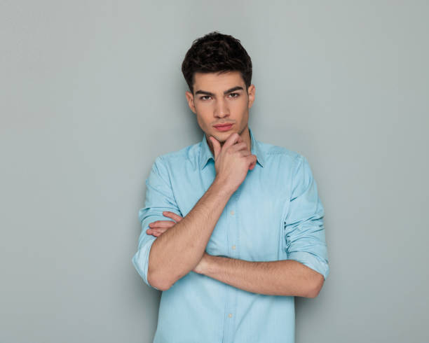istock confident young casual man folding arms, touching chin and thinking 1992148884