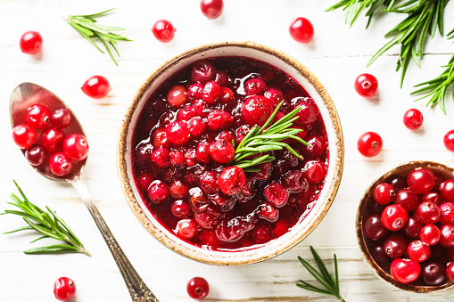 Cranberry sauce in craft bowl with rosemary. Top view at white table.