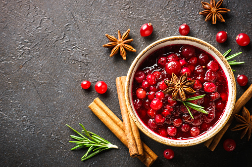 Cranberry sauce in a bowl with rosemary and spices. Top view at black background.