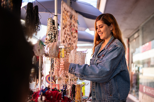 Young woman looking for necklace at market store