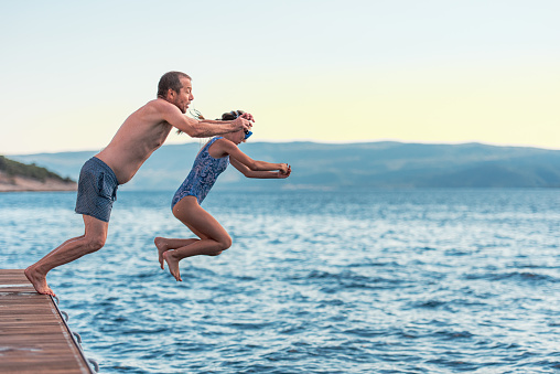 Teenage Girl on Seaside Holiday Having Fun with Father Jumping into the Sea