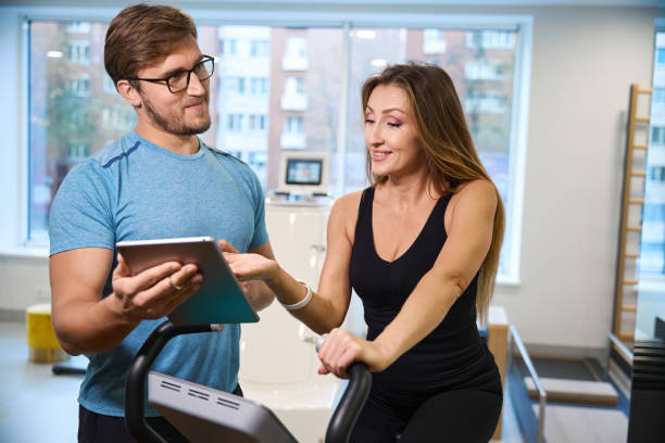 istock Young trainer communicates with a woman on an exercise bike 1992196340
