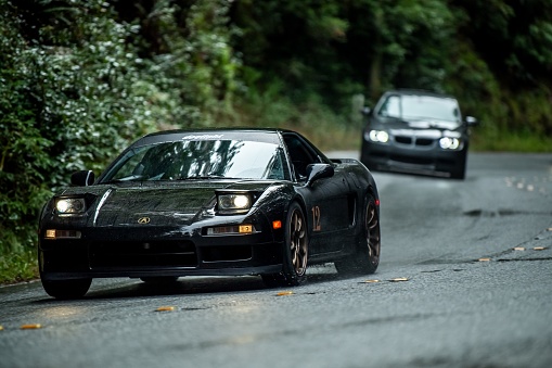 Woodside, United States – December 02, 2023: A Black Acura NSX driving on a road in the woods on a rainy day with BMW car in the background