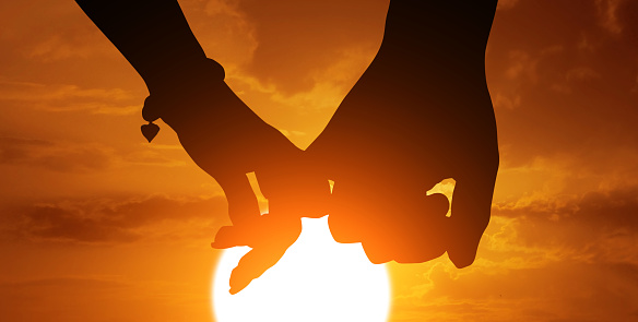 Silhouette of couple's arms holding hands at sunset. Celebrate Valentines Day.