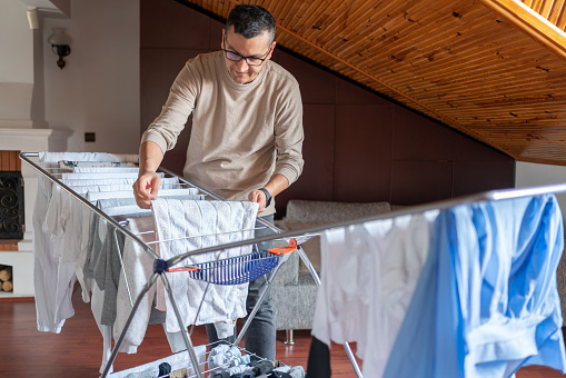 Man Hanging Clean Laundry On Drying Rack In Room