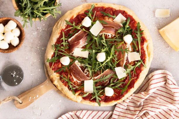 Pizza with Iberian ham, arugula, mozzarella and tomato on a wooden board.