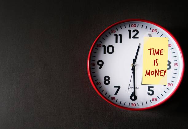 istock Red clock on gray copy space wall with note written TIME IS MONEY, time is precious to earn money , should spend it wisely and using time with compound interest investment , wealth can grow over time 1992225672