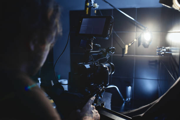 istock Video production backstage. Behind the scenes of creating video content, a professional team of cameramen with a director filming commercial ads. Video content creation, video creation industry. Low key, selective focus, film graine 1992240134