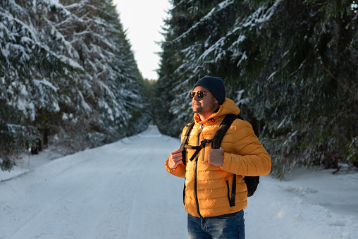 Portrait of a man with yellow jacket and sunglasses looking confident towards the sun on a scenic mountain road on a winter day