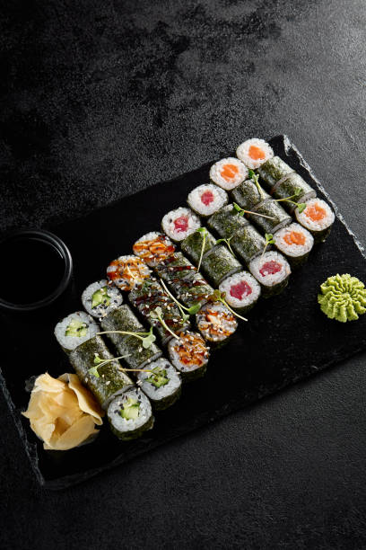 istock Assorted hosomaki sushi set with salmon, tuna, eel, and cucumber on black textured background 1992247361