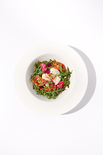 Top view of Italian salad with burrata, tomatoes, and arugula garnished with edible flowers.