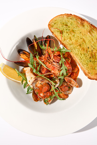 SautÃ©ed seafood medley in tomato sauce with a side of ciabatta toast on a white plate, top view for a delightful seafood experience.
