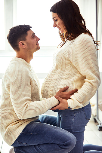 Close up portrait of expecting teenage couple laughing happily, embracing baby in belly together. Couple dressed in blue and white colors