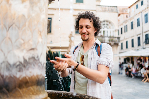 Young male tourist washing his hands in a fountain in Dubrovnik in Croatia.