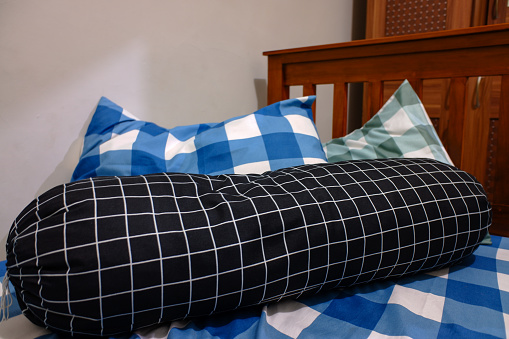 A mattress, pillow and bolster with checkered sheets in the bedroom.