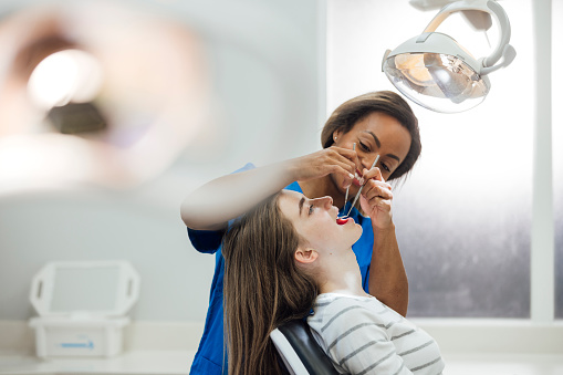 A side view of a young teenage girl who is sitting in the dentists chair for a hygienists appointment to check on the progress of her teeth. The hygenist is using the dental mirror check her back teeth. She is sitting in a private practice in the North East of England