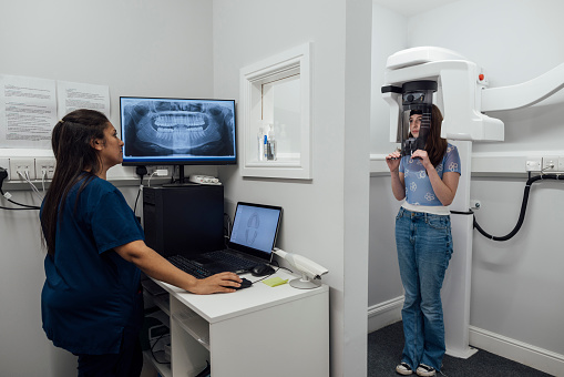 An over the shoulder wide angle view of a young teenage girl who is having dental scans taken to do some comparisons of how her teeth are progressing with her treatment. She is stood in a dental practice in the North East of England.