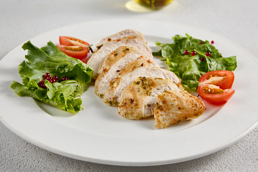 Grilled chicken breast with vibrant salad garnish on a minimalistic white setup, perfect for clean eating and diet concepts.