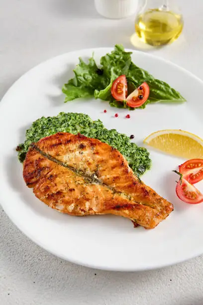 Pan-seared salmon steak with fresh spinach on white plate, perfect for healthy lifestyle and seafood cuisine presentations.