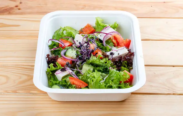Photo of Greek salad with feta cheese. Healthy diet.Takeaway food. On a wooden background.
