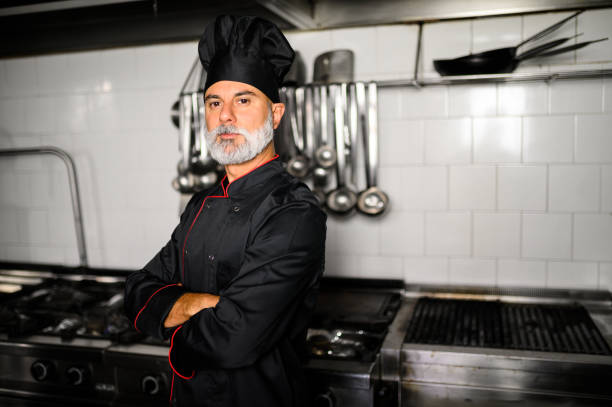 istock Mature chef in black coat with folded arms in his kitchen 1992277582