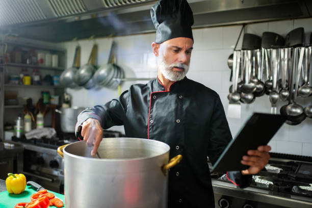 Professional chef cooking and reviewing recipe on tablet in kitc