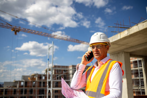 istock At the construction site, mid-adult Caucasian engineer talking on mobile phone while holding a blueprint 1992279244