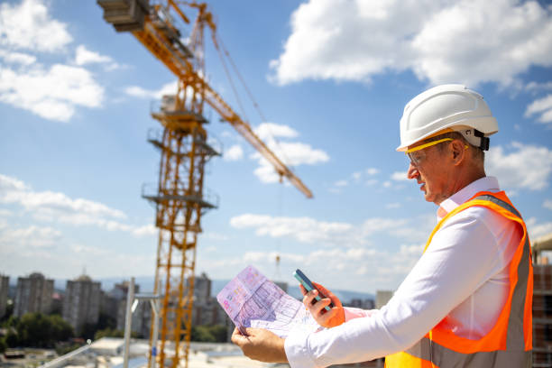 istock On the construction site, mid-adult Caucasian engineer using mobile phone and holding blueprint 1992279245