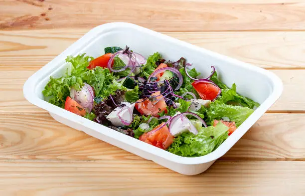 Photo of Greek salad with feta cheese. Healthy diet.Takeaway food. On a wooden background.