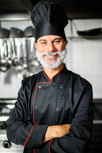 istock Mature chef in black coat with folded arms in his kitchen 1992280392
