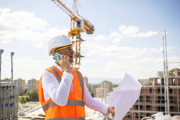 istock Side-view of an mid-adult Caucasian engineer talking on mobile phone while holding a blueprint on a construction site 1992281483