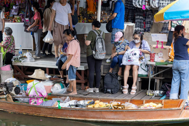 Bangkok, Thailand - June, 23rd 2013: Scene at Kwan Riam Floating Market in district Min Buri. People are walking over bridge connecting bth sides of floating market. At left side is temple. View over river and canal.