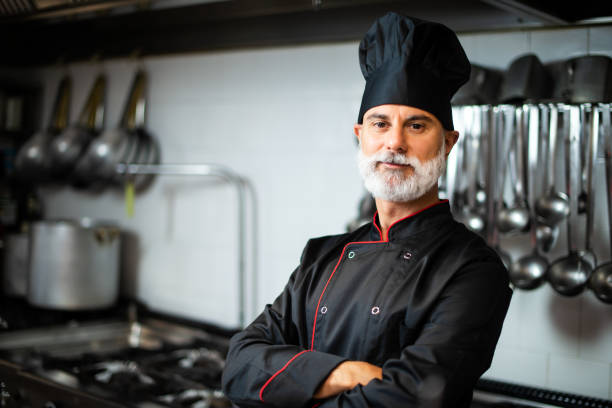 istock Mature chef in black coat with folded arms in his kitchen 1992283106