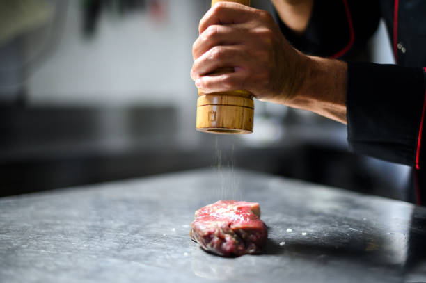 istock Chef pouring pepper on a raw steak to season it 1992284212