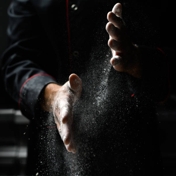 Closeup of chef's hands sprinkling flour, dark background