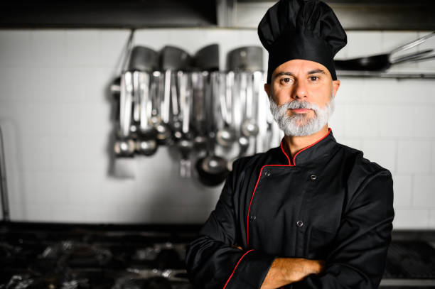 istock Mature chef in black coat with folded arms in his kitchen 1992286398