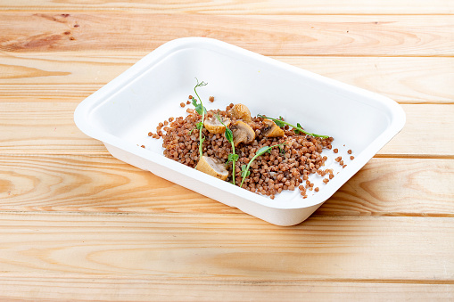 Buckwheat porridge with mushrooms. Healthy food. Takeaway food.  On a wooden background.