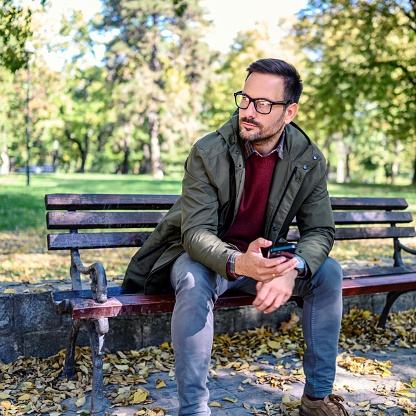 Man sitting at park bench and using smartphone