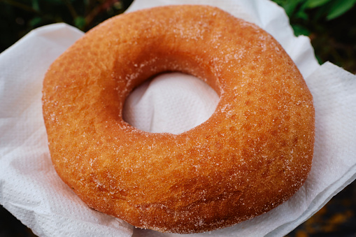Close up of a large ring doughnut on a white napkin outdoors.