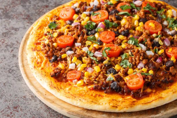istock Spicy Mexican Taco pizza with ground beef, tomatoes, corn, black beans, cheddar cheese, red onion on the wooden board. Horizontal 1992329584