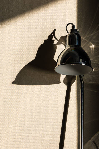 A black table lamp placed next to a window with sunlight streaming in.