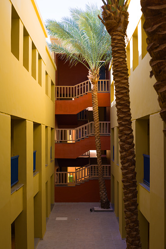View along corridors of two hotel buildings to the staircase next to tall palm tree in the courtyard