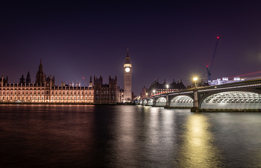 London. UK- 02.04.2024. A long exposure night time view of the Palace of Westminster, Big Ben and Westminster Bridge casting light reflections on the river Thames.