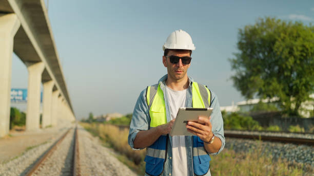 istock Male foreman engineer wearing helmet and safety vest using tablet working on railway. Engineer checking construction process railway on tablet. Transportation, Engineer leadership concept 1992362297